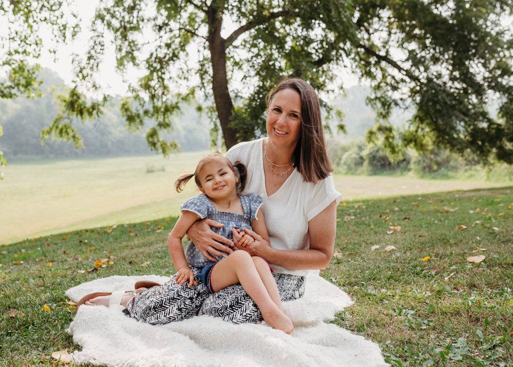 woman with daughter on lap sitting on grassy hill