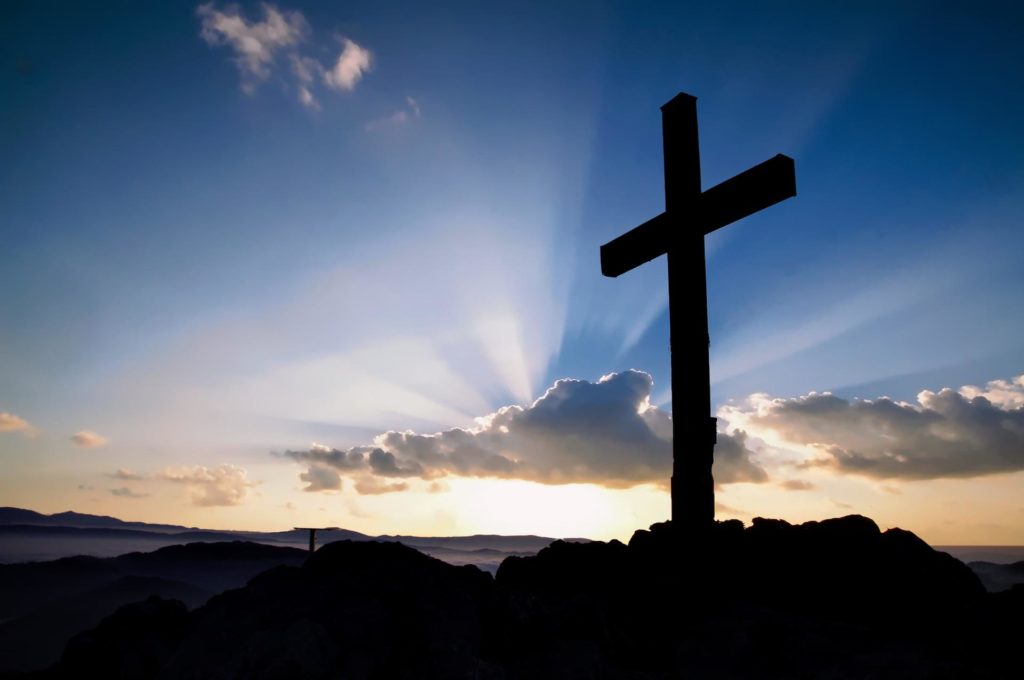 cross on a hill with the sunrise in the background